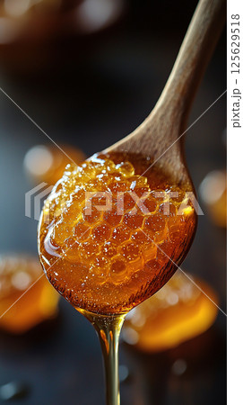 A wooden spoon holds fresh honeycomb, dripping with golden, sweet honey, macro shot. 125629518