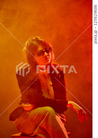 Woman in blazer and sunglasses stares into distance 125629686