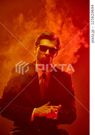 Man folding hands in front of chest with blank stare surrounded by fire-hued fog. Concept of business, economic depression. Man folding hands in front of chest with blank stare surrounded by fire-hued fog. Concept of business, economic depression. 125629694