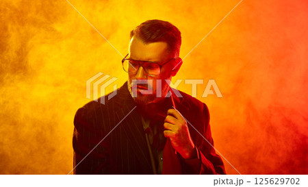 Man in pinstripe suit adjusts tie with firm expression amid thick orange fog symbolizing control under pressure 125629702