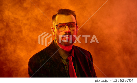 Man faces forward with emotionless gaze surrounded by orange smoke as if lost in deep thought 125629704