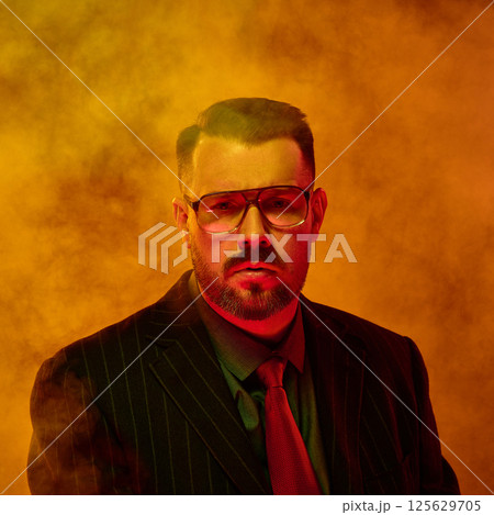 Confident man in striped suit and glasses stares intensely through thick yellow haze in tense moment 125629705
