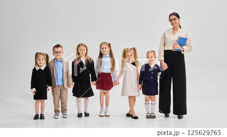Group of diverse children holding hands with female teacher in smart outfit standing nearby. Concept of unity, diversity 125629765