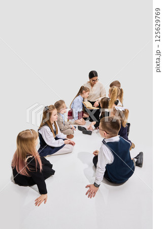 Children sitting in circle on floor with teacher reading storybook and showing page to group. Concept of storytelling, imagination Children sitting in circle on floor with teacher reading storybook and showing page to group. Concept of storytelling, imagination 125629769