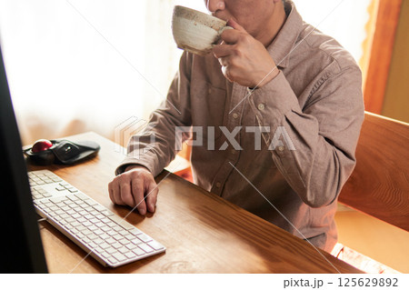 パソコンの画面を見ながら飲み物を飲む男性 125629892