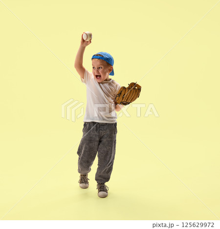 Happy boy holding baseball and glove smiling and shouting of joy against yellow background. 125629972