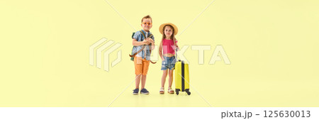 Banner. Stylish boy and girl standing with backpack and suitcase looking confident against yellow background with negative space. Banner. Stylish boy and girl standing with backpack and suitcase looking confident against yellow background with negative space. 125630013