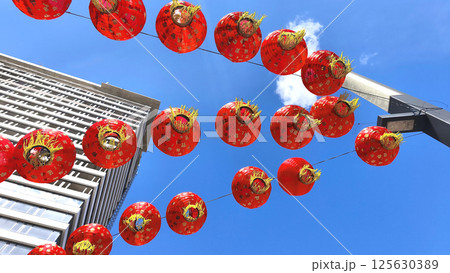 Garland of bright red Chinese lanterns against sky and modern city building, celebrating festive traditions in oriental style. 125630389