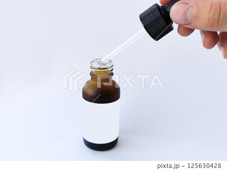 Brown dropper bottle with blank label and pipette held by hand, ideal for skincare, essential oils, medicine, or cosmetic product mockups and advertising. Brown dropper bottle with blank label and pipette held by hand, ideal for skincare, essential oils, medicine, or cosmetic product mockups and advertising. 125630428