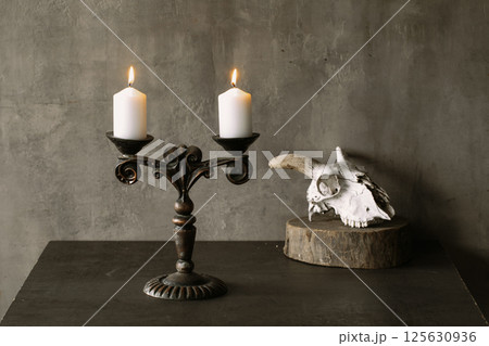 Beautiful vintage brass candelabrum with two burning candles and goats skull in the dark, atmospheric image. 125630936