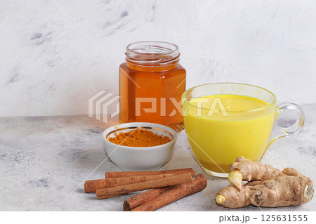 Healthy drink of golden turmeric latte with ginger root, cinnamon sticks, turmeric powder and honey, spices for Ayurvedic medicine. Alternative medicine concept, has a strong anti-inflammatory effect, Healthy drink of golden turmeric latte with ginger root, cinnamon sticks, turmeric powder and honey, spices for Ayurvedic medicine. Alternative medicine concept, has a strong anti-inflammatory effect, 125631555