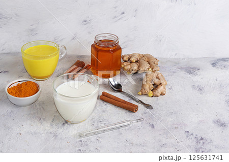 Healthy drink of golden turmeric latte with ginger root, cinnamon sticks, turmeric powder, a cup of milk and honey, spices for Ayurvedic medicine. Alternative medicine concept, has a strong Healthy drink of golden turmeric latte with ginger root, cinnamon sticks, turmeric powder, a cup of milk and honey, spices for Ayurvedic medicine. Alternative medicine concept, has a strong 125631741