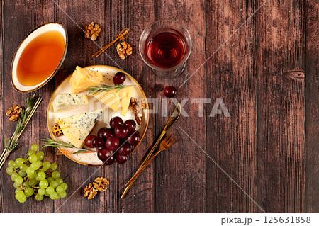 Still life with gourmet blue cheese, parmesan, grapes, honey, nuts, rosemary and wine. Top view of cheese plate with seasonal wine appetizers, Italian cuisine concept, restaurant and cafe menu. Still life with gourmet blue cheese, parmesan, grapes, honey, nuts, rosemary and wine. Top view of cheese plate with seasonal wine appetizers, Italian cuisine concept, restaurant and cafe menu. 125631858