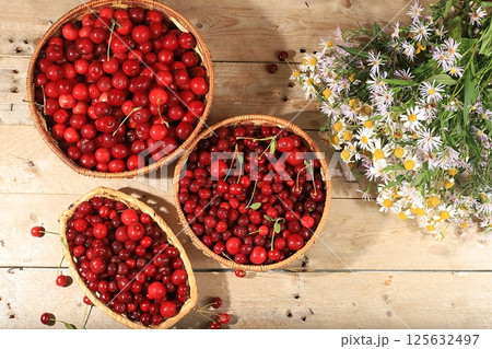 Summer cherry berries in baskets on a wooden background with daisies,wild flowers, harvesting in the village, the concept of healthy natural food, breakfast with ingredients, shop advertising, cafe 125632497