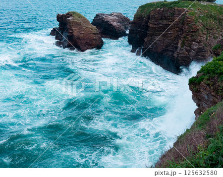 Dramatic ocean waves crashing against rocky cliffs with turquoise waters 125632580