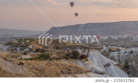 People watching a beautiful sunrise with colorful hot air balloons flying in clear morning sky aerial timelapse in Cappadocia, Turkey 125633762