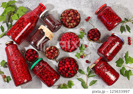 Jars with raspberry, cherry, gooseberry jam and compote on a light background with leaves and fresh berries, home canning concept, banner and advertising of a store and market, village harvest, 125633997