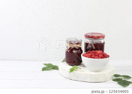 Village harvest, jars of raspberry jam on light wooden background with leaves, shop banner and advertisement, healthy natural food concept, breakfast 125634003