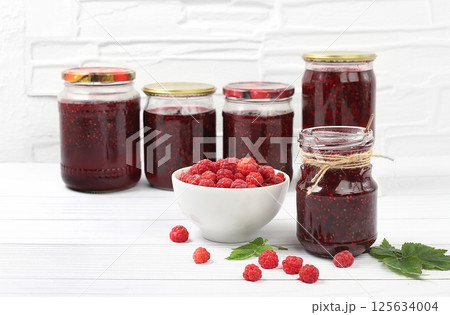 Jars of raspberry jam on a light wooden background with leaves, banner and shop advertisement, healthy natural food concept, home canning concept, Village harvest, breakfast with ingredients, 125634004
