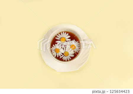 Chamomile tea in a cup with natural small chamomile flowers on a light table, the concept of herbal tea and proper natural nutrition, summer postcard, selective focus Chamomile tea in a cup with natural small chamomile flowers on a light table, the concept of herbal tea and proper natural nutrition, summer postcard, selective focus 125634423