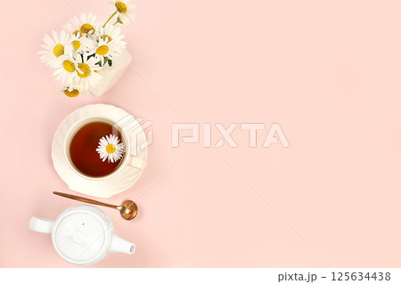 Chamomile tea in a cup with natural small chamomile flowers and a teapot on a light table, a minimal concept of herbal tea and proper natural nutrition, summer postcard, top view, selective focus 125634438