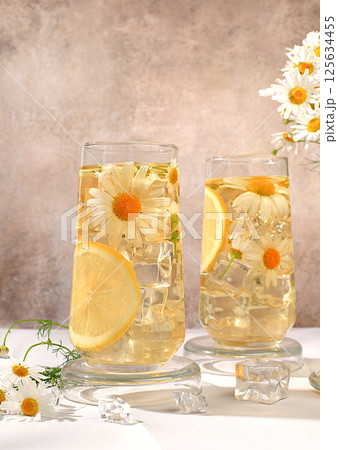 Chamomile tea with lemon in transparent glasses with natural small chamomile flowers on a rustic table, concept of medicinal herbal tea and proper natural nutrition, summer card, 125634455