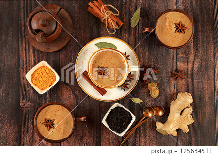 Indian masala chai tea with milk, ginger, anise and cinnamon on an old wooden table. Traditional drink with spices, cafe concept, advertising for restaurant and menu. Selective focus Indian masala chai tea with milk, ginger, anise and cinnamon on an old wooden table. Traditional drink with spices, cafe concept, advertising for restaurant and menu. Selective focus 125634511