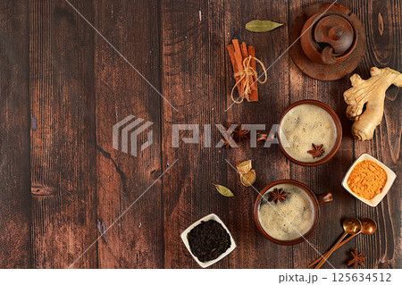 Indian masala chai tea with milk, ginger, anise and cinnamon on an old wooden table. Traditional drink with spices, cafe concept, advertising for restaurant and menu. Selective focus Indian masala chai tea with milk, ginger, anise and cinnamon on an old wooden table. Traditional drink with spices, cafe concept, advertising for restaurant and menu. Selective focus 125634512