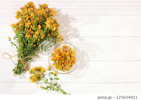 Collection of useful herbs for treatment according to folk recipes. Bouquet of fresh Hypericum flowers and dried petals in a cup on a wooden table, alternative traditional medicine concept, 125634921