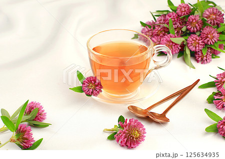 Medicinal herbal tea or infusion of red clover in a glass cup with flowers, alternative traditional medicine concept, estrogen source, menopause remedy, advertising for green pharmacy, 125634935