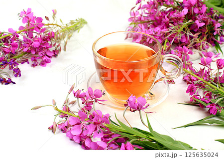 Medicinal herbal tea or fireweed infusion in a glass cup with flowers, the concept of alternative traditional medicine, green pharmacy advertising, collection of useful herbs for treatment according 125635024