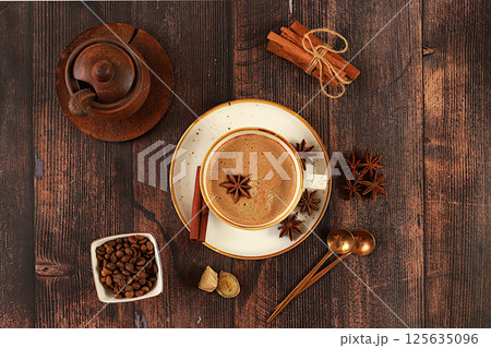 Cup of coffee with milk, ginger, anise and cinnamon on an old wooden table. Traditional Indian drink with spices, cafe concept, advertising for restaurant and menu. Selective focus 125635096