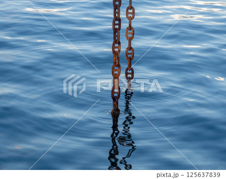 Powerful metal chain going into the water. Deep sea work. An industrial tool lowered into the depths of the sea Powerful metal chain going into the water. Deep sea work. An industrial tool lowered into the depths of the sea 125637839