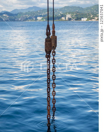 Powerful metal chain going into the water. Deep sea work. An industrial tool lowered into the depths of the sea. 125637841