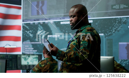 American military intelligence officers in a command center monitoring surveillance information in order to safeguard state secrets. Managing security in an army base of operations. Camera A. American military intelligence officers in a command center monitoring surveillance information in order to safeguard state secrets. Managing security in an army base of operations. Camera A. 125638222