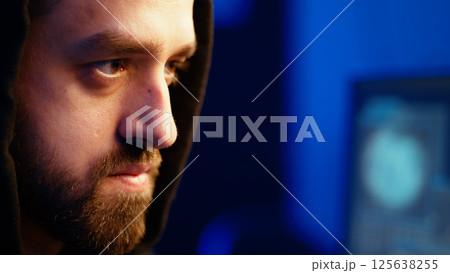 Malicious man hacking, stealing credit card numbers and manipulating banking systems for his own personal gain. Extreme close up of rogue programmer running code in graffiti painted basement, camera A 125638255