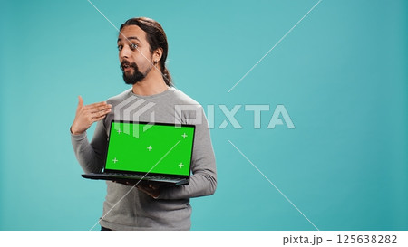 Tech content creator doing influencer marketing using green screen laptop, isolated over studio background. Arab man holding empty copy space mockup notebook, doing review, camera B Tech content creator doing influencer marketing using green screen laptop, isolated over studio background. Arab man holding empty copy space mockup notebook, doing review, camera B 125638282