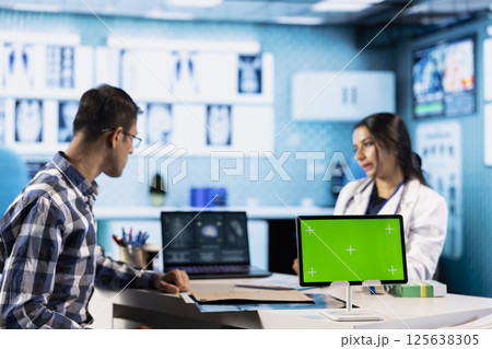 Specialist discussing x ray imaging with a patient next to isolated mockup display, presenting healthcare diagnosis during check up visit. Physician sharing the treatment plan and advice. 125638305