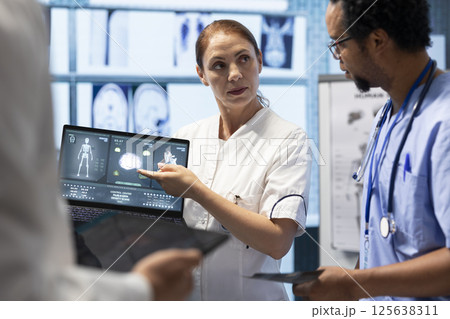 Medical team examining x ray scan results to discuss patient care options. Group of licensed cardiologists analyzing cardiac issues on a ecg radiography, effective treatment in a clinic. 125638311