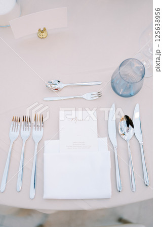 Personalized invitation lies in a white napkin on the table next to the cutlery, opposite a blank card on a stand Personalized invitation lies in a white napkin on the table next to the cutlery, opposite a blank card on a stand 125638956