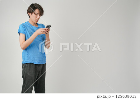 青シャツと黒のジョガーパンツを着た日本人男性が両手でスマートフォンを操作している 青シャツと黒のジョガーパンツを着た日本人男性が両手でスマートフォンを操作している 125639015