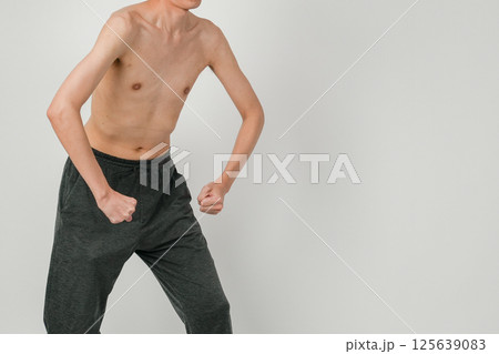 体の細さを強調しながらも筋トレへの意欲を見せるポーズを取る痩せ型男性の写真 125639083