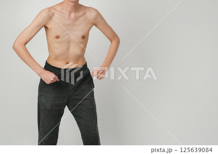 体の細さを強調しながらも筋トレへの意欲を見せるポーズを取る痩せ型男性の写真 125639084