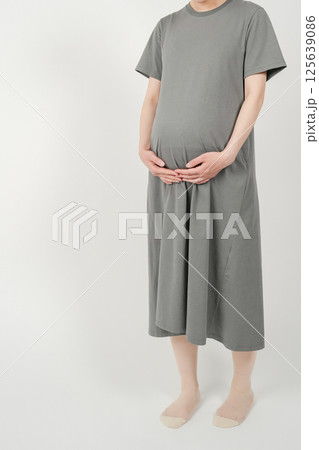 出産を控えた妊娠後期の日本人女性が立ち姿でお腹を両手で包み込む様子 125639086