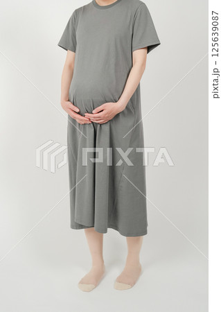 出産を控えた妊娠後期の日本人女性が立ち姿でお腹を両手で包み込む様子 125639087