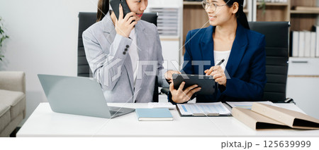 Businesswomen work and discuss their business plans. A women employee explains and shows her colleague in office. Businesswomen work and discuss their business plans. A women employee explains and shows her colleague in office. 125639999