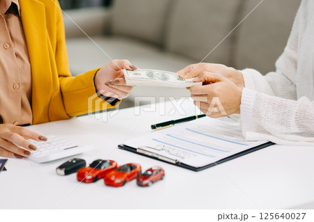 Asian people car salesman or sales manager offers to sell a car and explains of signing a car contract and signing car insurance document Asian people car salesman or sales manager offers to sell a car and explains of signing a car contract and signing car insurance document 125640027