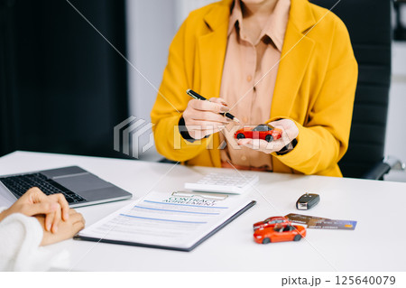 Asian people car salesman or sales manager offers to sell a car and explains of signing a car contract and signing car insurance document 125640079