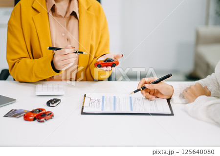 Asian people car salesman or sales manager offers to sell a car and explains of signing a car contract and signing car insurance document Asian people car salesman or sales manager offers to sell a car and explains of signing a car contract and signing car insurance document 125640080
