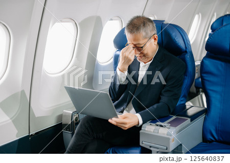 Photo of a frustrated senior man sitting on an airplane with her head in her hands. 125640837